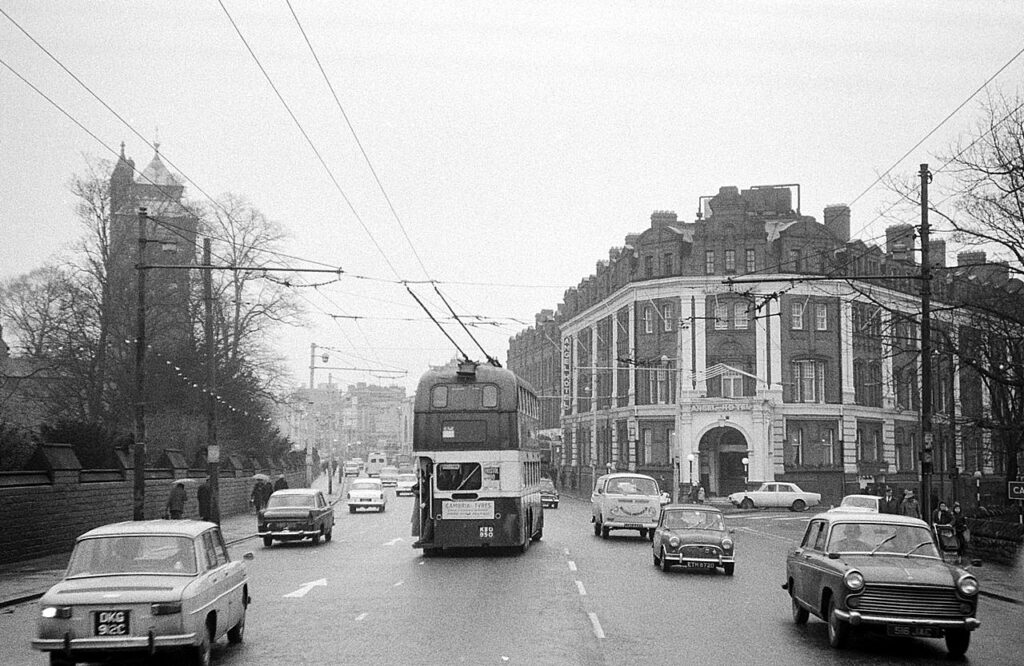 A trolleybus on a city street with hotel and castle in the background.